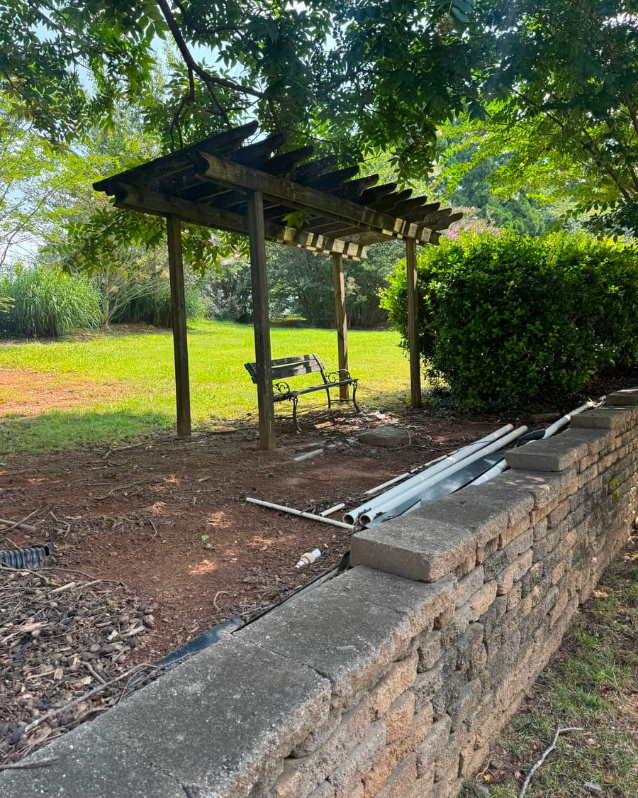 Muro de retención de bloque con línea de drenaje corrida por detrás, junto a una pérgola